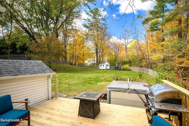 wooden terrace featuring a fire pit, grilling area, a hot tub, a storage unit, and a lawn