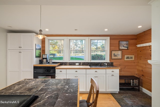 kitchen with white cabinetry, hanging light fixtures, a healthy amount of sunlight, and wood walls