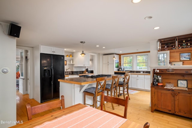 kitchen with a kitchen island, a kitchen breakfast bar, black fridge, decorative light fixtures, and white cabinets