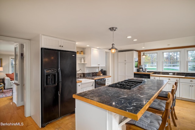 kitchen featuring a kitchen breakfast bar, sink, black appliances, a center island, and white cabinetry