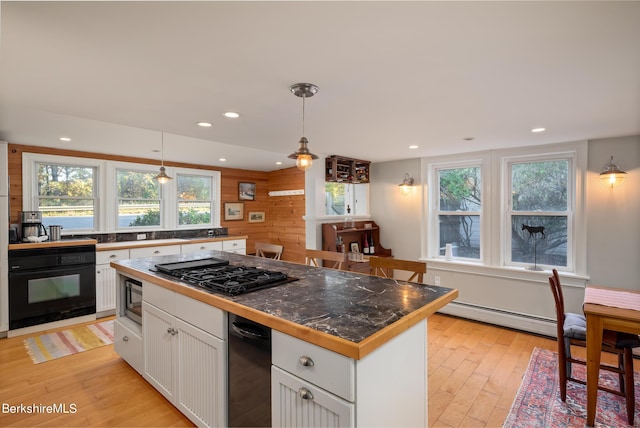 kitchen with plenty of natural light, white cabinets, black appliances, and decorative light fixtures