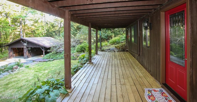 wooden deck featuring a lawn, a detached garage, and an outdoor structure