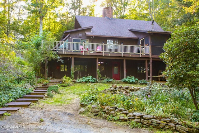 back of property with stairway, a chimney, a shingled roof, and a wooden deck