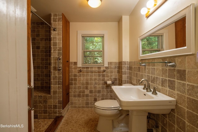 bathroom featuring tile patterned flooring, a tile shower, toilet, and tile walls