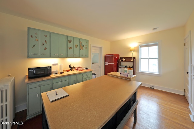 49 Main St, Stockbridge, MA 01262 - kitchen featuring green cabinetry, radiator heating unit, black microwave, wood finished floors, and light countertops