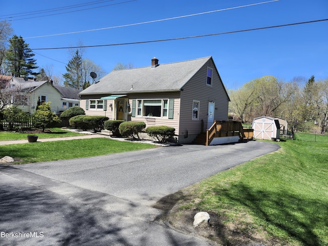 view of front facade with a storage unit, aphalt driveway, a front yard, a chimney, and an outdoor structure