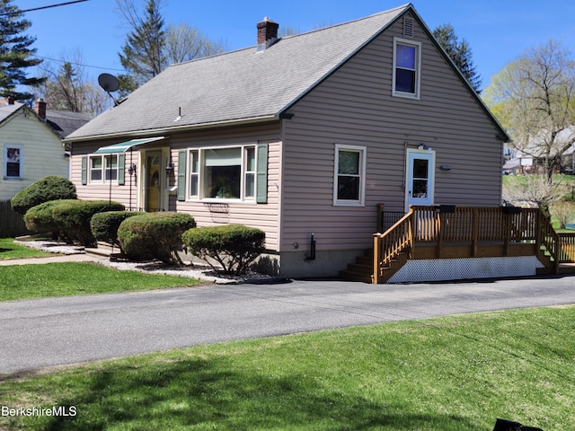 view of front facade with a front lawn, roof with shingles, a chimney, and a deck