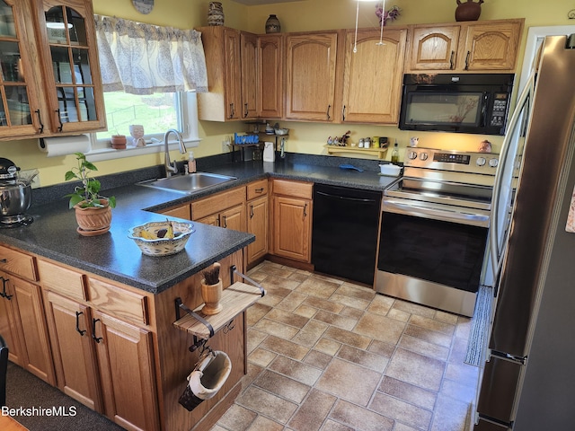 kitchen with dark countertops, a sink, stone finish flooring, glass insert cabinets, and black appliances