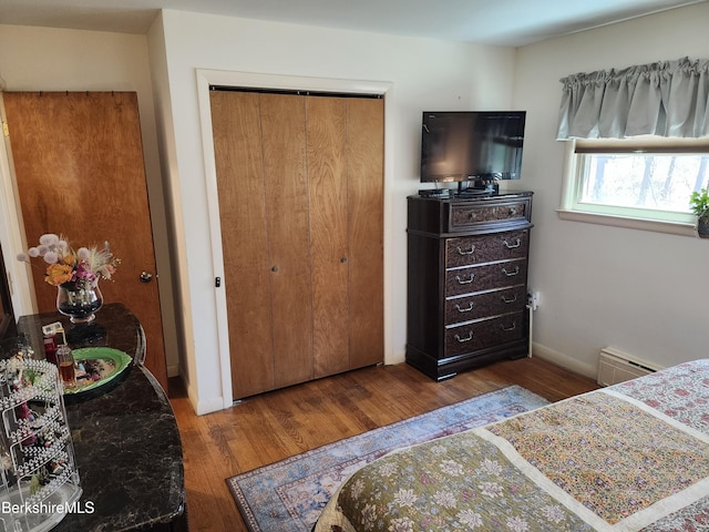 bedroom with baseboards, baseboard heating, a closet, and wood finished floors
