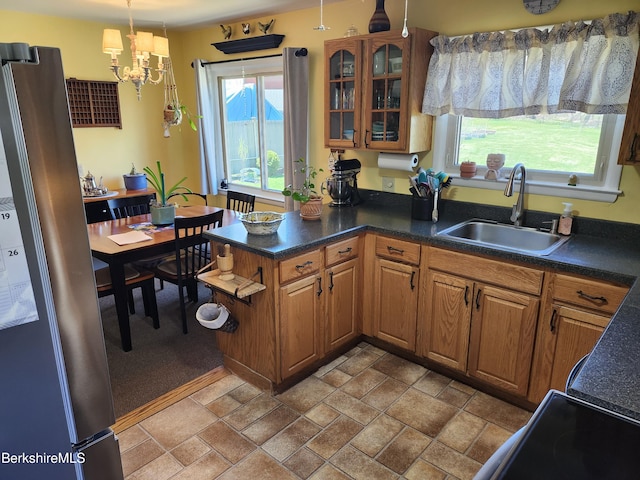 kitchen featuring dark countertops, a sink, freestanding refrigerator, a peninsula, and a chandelier
