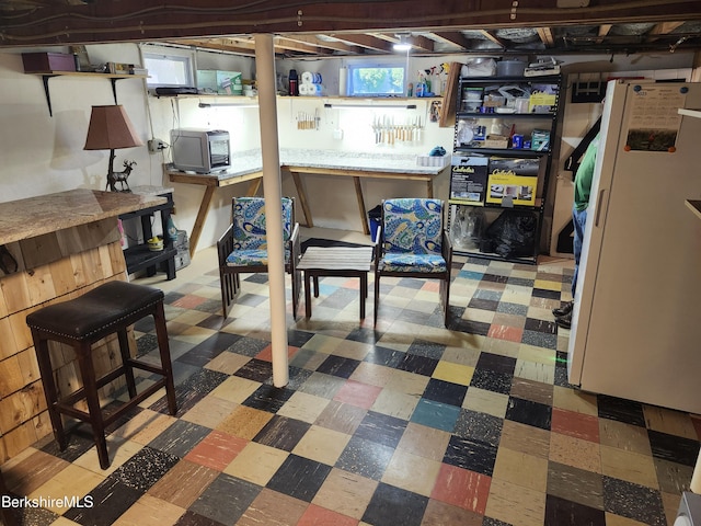 below grade area featuring tile patterned floors and freestanding refrigerator