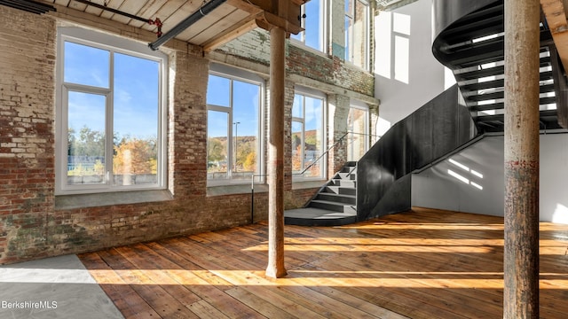 interior space featuring a towering ceiling, brick wall, and wood-type flooring