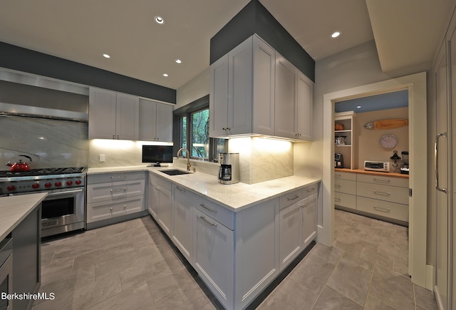 kitchen featuring wall chimney exhaust hood, white cabinetry, high end stainless steel range, and tasteful backsplash