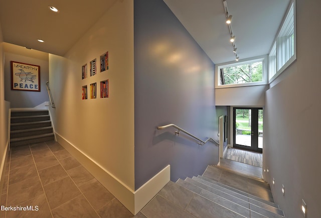 stairway with french doors, a towering ceiling, track lighting, and tile patterned floors