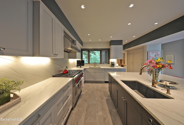 kitchen featuring light stone countertops, range with two ovens, wall chimney range hood, and sink