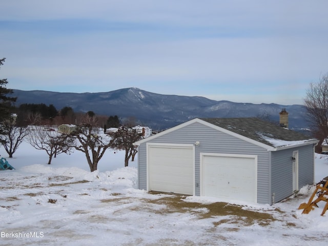 snow covered garage featuring a detached garage and a mountain view