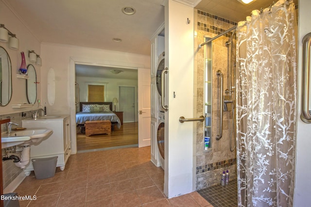 bathroom with stacked washing maching and dryer, ornamental molding, sink, tiled shower, and tile patterned flooring