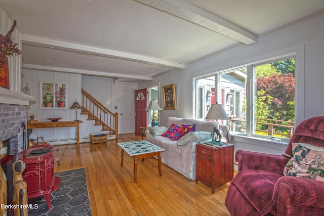 living room featuring beam ceiling, light hardwood / wood-style floors, a brick fireplace, and baseboard heating