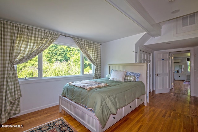 bedroom with multiple windows, hardwood / wood-style floors, and beamed ceiling