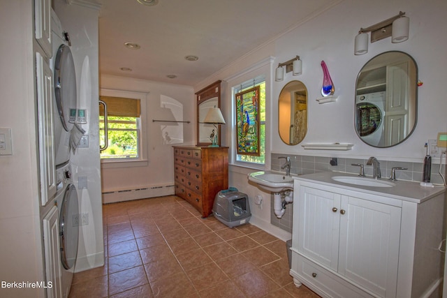 bathroom featuring stacked washing maching and dryer, tile patterned flooring, a baseboard heating unit, crown molding, and dual sinks