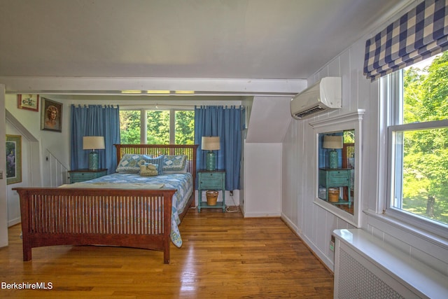 bedroom with an AC wall unit, radiator heating unit, and hardwood / wood-style floors