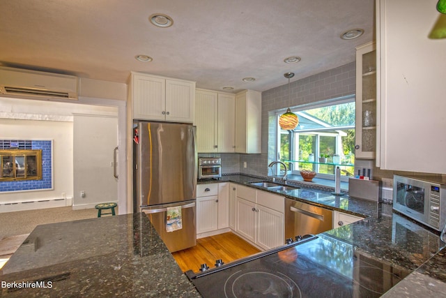 kitchen with a wall unit AC, white cabinetry, sink, and stainless steel appliances