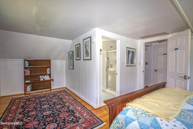 bedroom featuring ensuite bathroom, light hardwood / wood-style flooring, lofted ceiling, and wooden walls