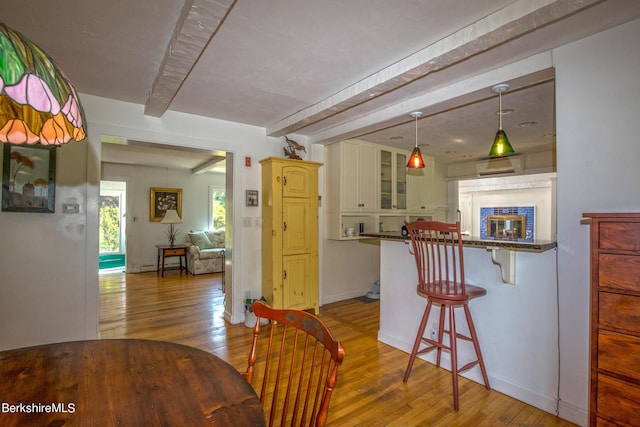 interior space featuring hanging light fixtures, light hardwood / wood-style flooring, beamed ceiling, a breakfast bar, and white cabinets