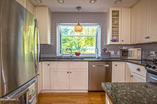 kitchen with dark stone counters, sink, hanging light fixtures, decorative backsplash, and stainless steel appliances