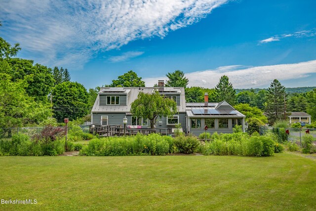 rear view of property with solar panels, a wooden deck, and a lawn