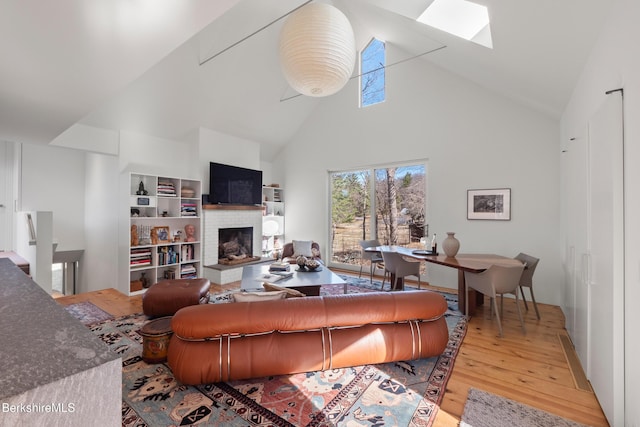 living area featuring a skylight, high vaulted ceiling, a brick fireplace, and wood finished floors