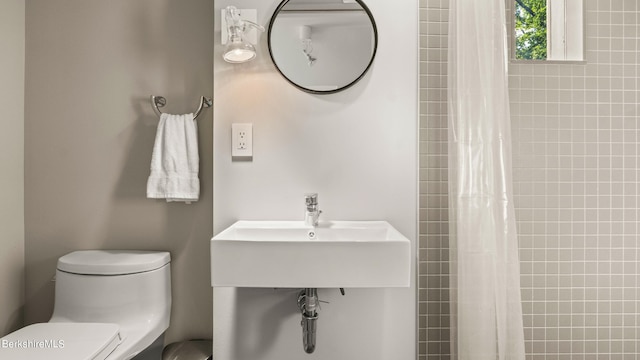bathroom featuring a sink, toilet, and a tile shower