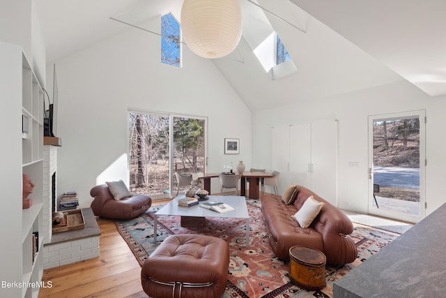 living room featuring high vaulted ceiling, a brick fireplace, hardwood / wood-style flooring, and a skylight