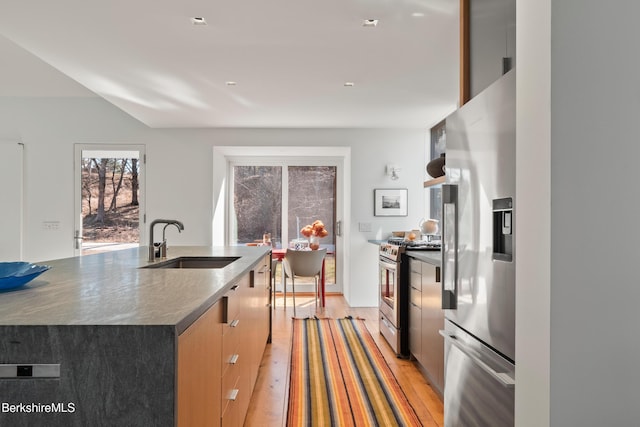 kitchen with light wood-type flooring, a center island with sink, modern cabinets, appliances with stainless steel finishes, and a sink