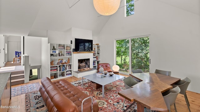 living area with high vaulted ceiling, a brick fireplace, and wood finished floors