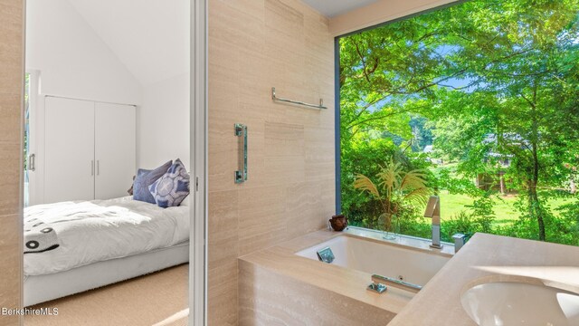 ensuite bathroom with lofted ceiling, ensuite bathroom, a sink, and a tub with jets