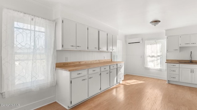 kitchen with light wood finished floors, baseboards, white cabinets, a wall mounted AC, and a sink