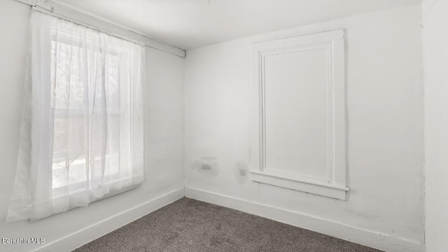 unfurnished room featuring dark colored carpet, baseboards, and plenty of natural light