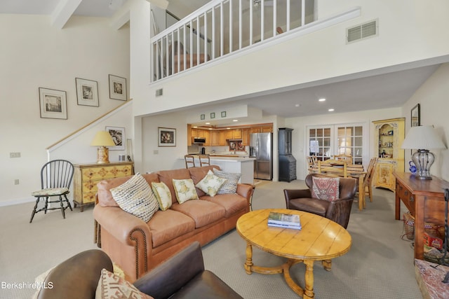 living room with a towering ceiling, light colored carpet, and beamed ceiling