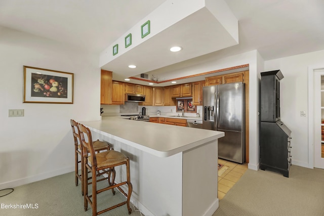 kitchen with light colored carpet, a breakfast bar area, stainless steel appliances, and kitchen peninsula