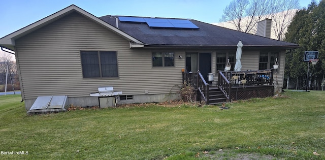 rear view of property with a lawn, a wooden deck, and solar panels