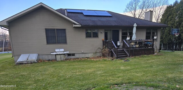 back of property with a yard, roof with shingles, solar panels, and a chimney