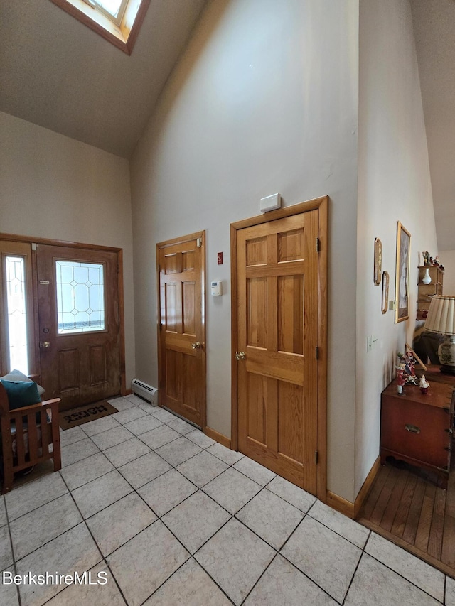 foyer with high vaulted ceiling, light tile patterned flooring, a skylight, and a baseboard radiator