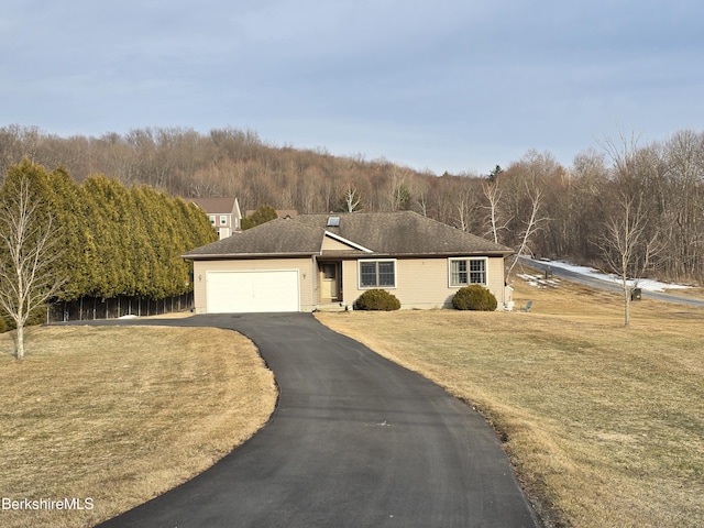 single story home with a front yard, a garage, a wooded view, and aphalt driveway