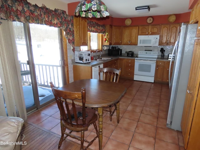 kitchen with a sink, tasteful backsplash, white appliances, light tile patterned flooring, and brown cabinetry