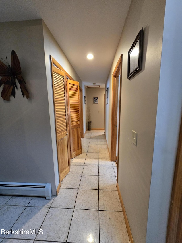 hall with a baseboard heating unit, light tile patterned floors, and baseboards