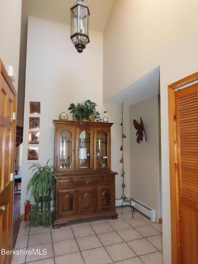 foyer entrance featuring light tile patterned floors, a baseboard heating unit, and a high ceiling