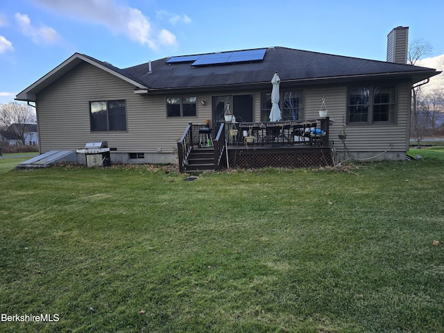 back of property with a chimney, a lawn, solar panels, and a wooden deck