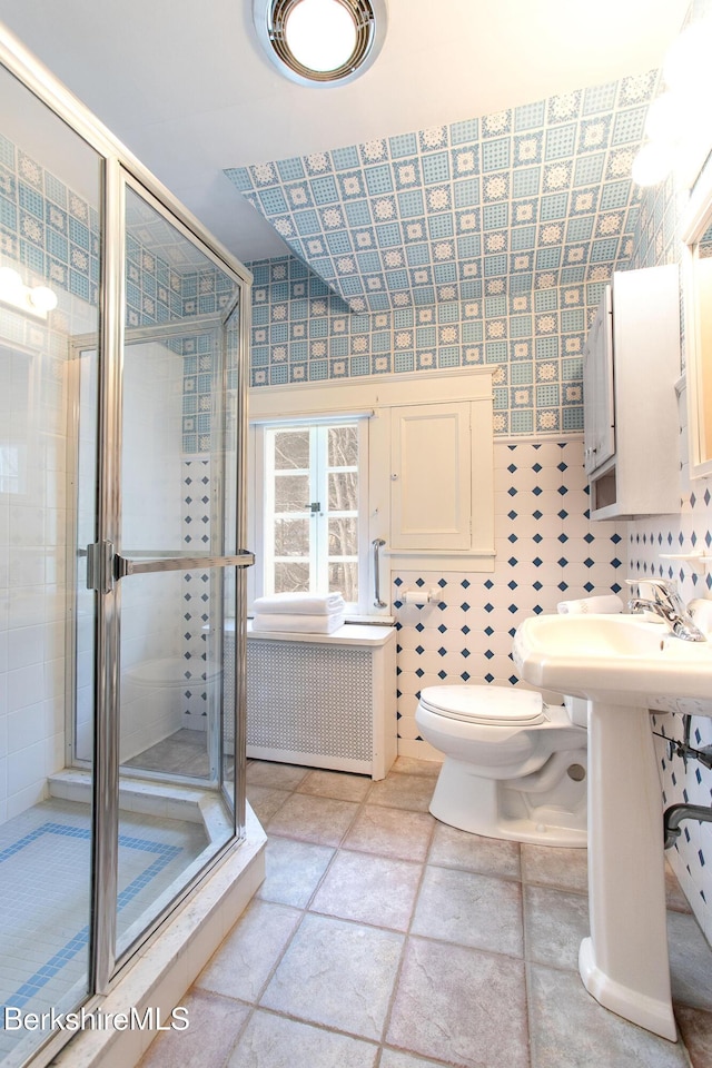 bathroom with radiator, wallpapered walls, a sink, a shower stall, and toilet