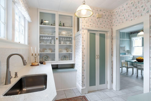 kitchen with wallpapered walls, light tile patterned flooring, a wealth of natural light, and a sink